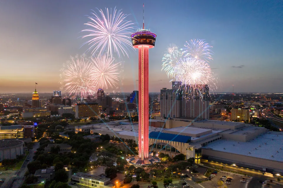 Tower of the Americas lit red with fireworks over downtown San Antonio at night