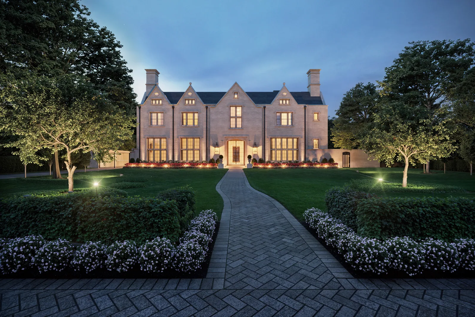 Del Monte limestone home in Houston lit at dusk at the end of a herringbone garden walk