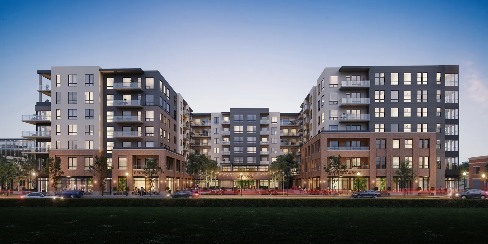 Brick and gray-panel mixed-use buildings of Encore in Castle Rock seen across a lawn in the evening