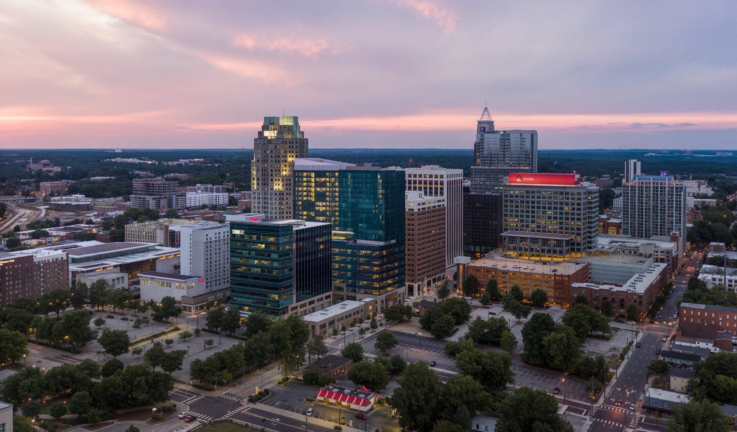 501 Fayetteville St Raleigh skyline aerial architectural rendering by Bogza.com. A stunning twilight drone view over downtown Raleigh, North Carolina, showcasing the modern 22-story FNB Tower's illuminated glass crown alongside the BB&T and Red Hat buildings.