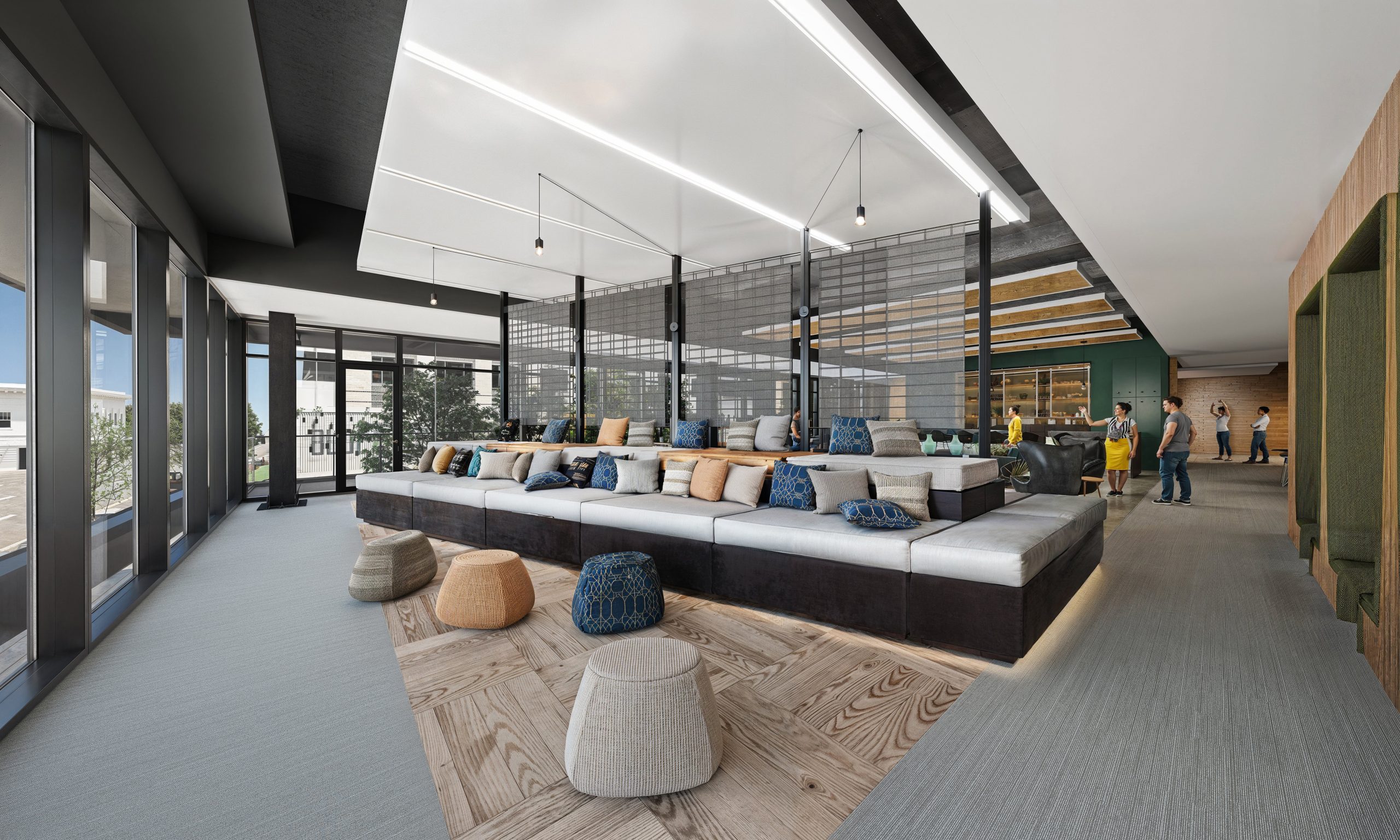 621 Hillsborough Raleigh coworking lounge interior rendering by Bogza.com. A bright, modern communal office space featuring a large custom tiered sofa with blue throw pillows, wood-paneled ceiling baffles, and large windows looking out over downtown Raleigh.