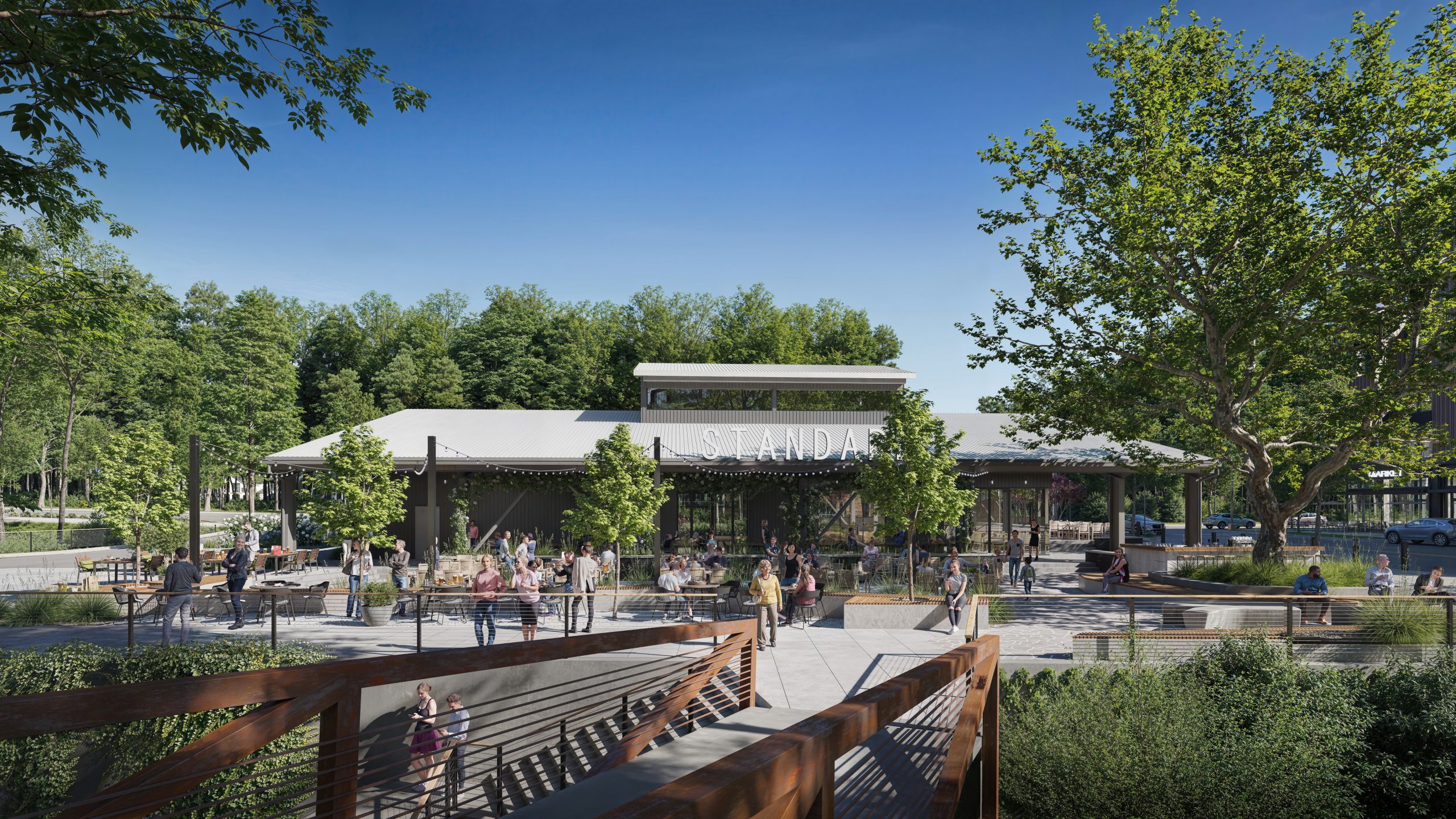 Standard Beer + Food at NHID Raleigh exterior architectural rendering by Bogza.com. A bright daytime view of the freestanding restaurant space, featuring an expansive outdoor gathering patio, modern landscaping, a rust-colored steel pedestrian bridge, and active community members enjoying the greenway connections.