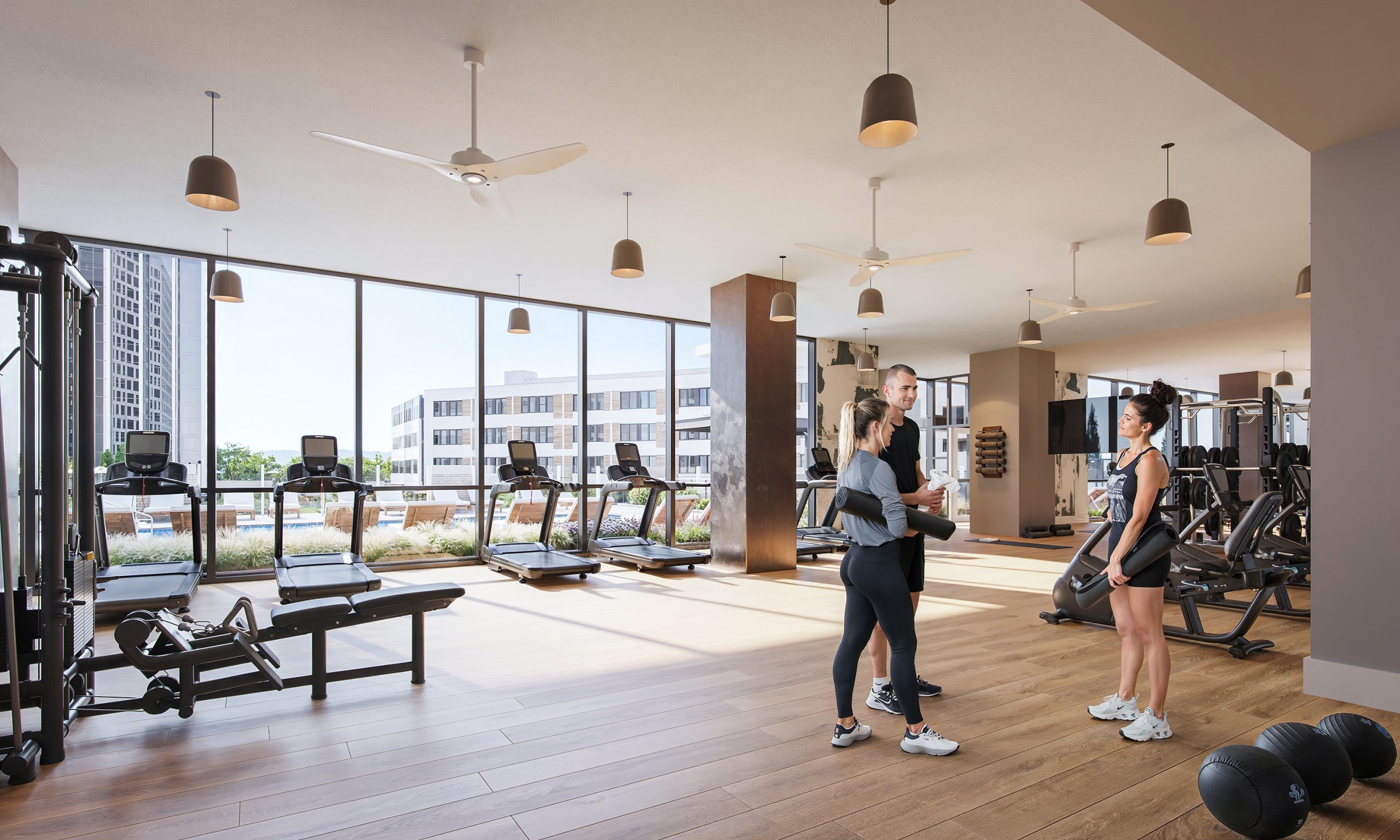 Salisbury Square Raleigh luxury apartment fitness center interior rendering by Bogza.com. A bright, state-of-the-art gym amenity space featuring warm wood flooring, cardio treadmills, free weights, and expansive floor-to-ceiling windows overlooking the outdoor pool terrace.