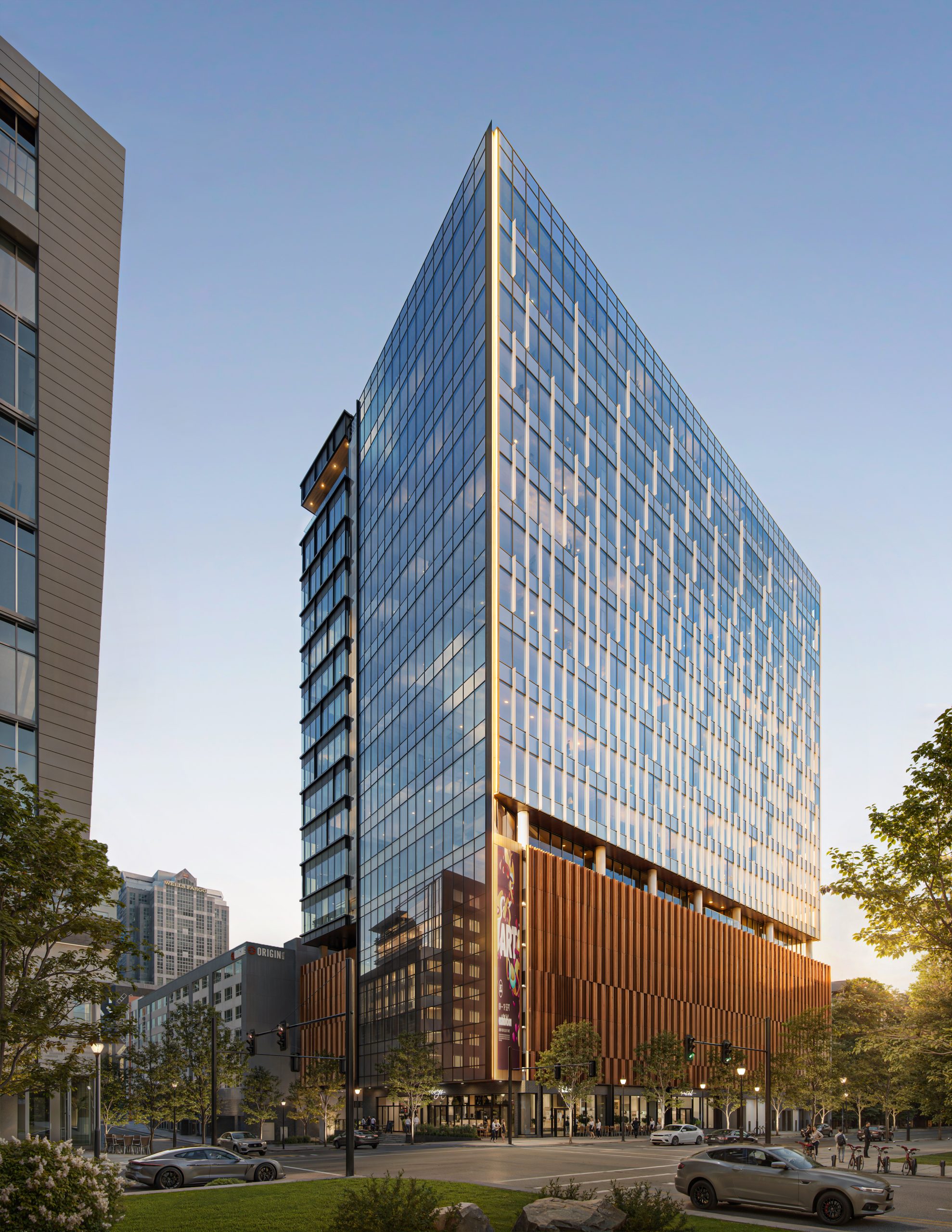 Tower 3 at Bloc 83 Raleigh mixed-use exterior architectural rendering by Bogza.com. A bright daytime corner view of the 18-story modern glass office tower, showcasing its sleek facade, an integrated parking deck featuring vertical wood fins, and ground-floor retail spaces along the streetscape.