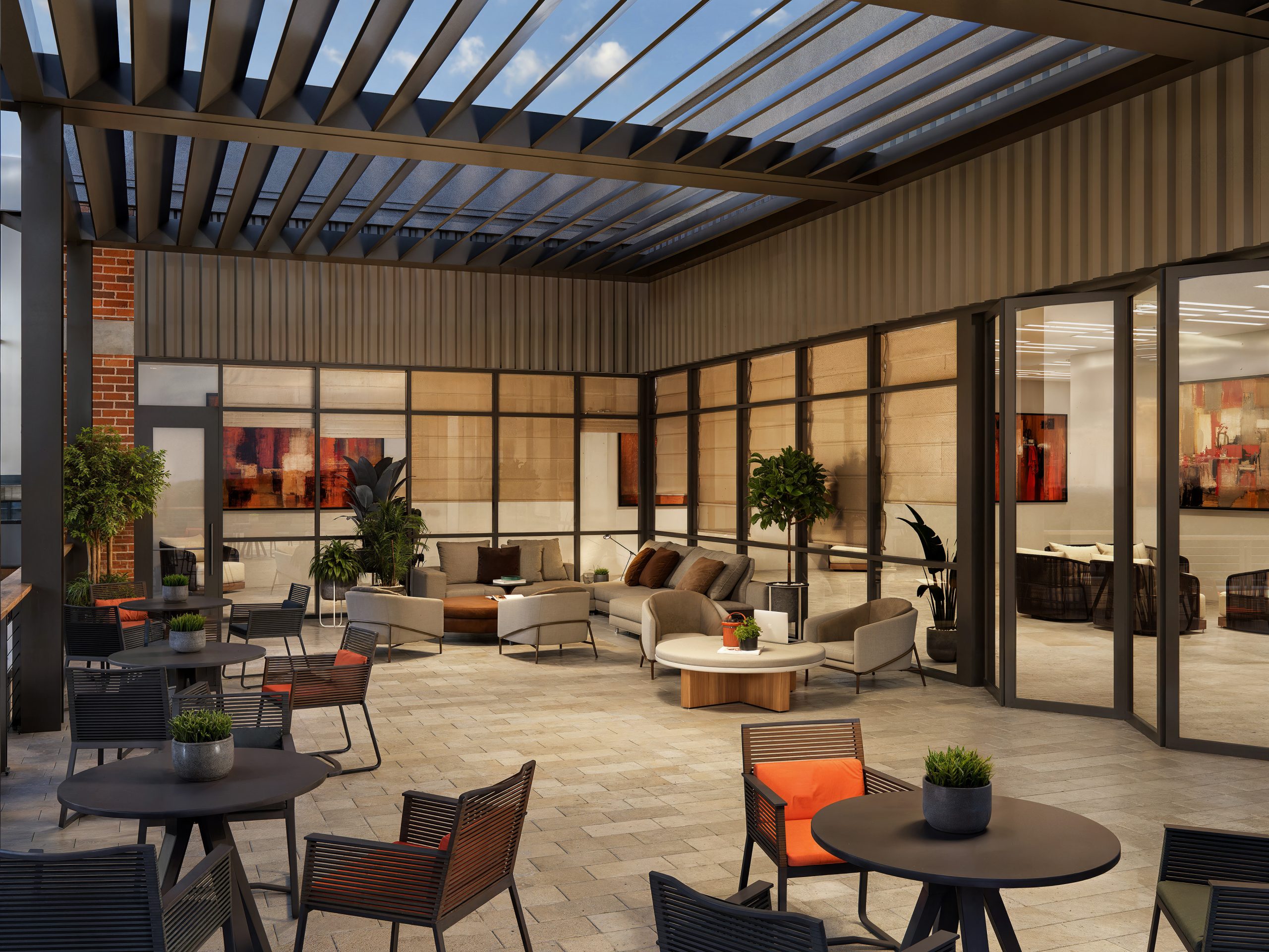 The Station at LoSo Charlotte office outdoor terrace amenity rendering by Bogza.com. A bright daytime view of an elevated outdoor tenant deck, featuring a modern louvered pergola, comfortable lounge seating, dark metal planters, and folding glass doors connecting to the indoor office space.