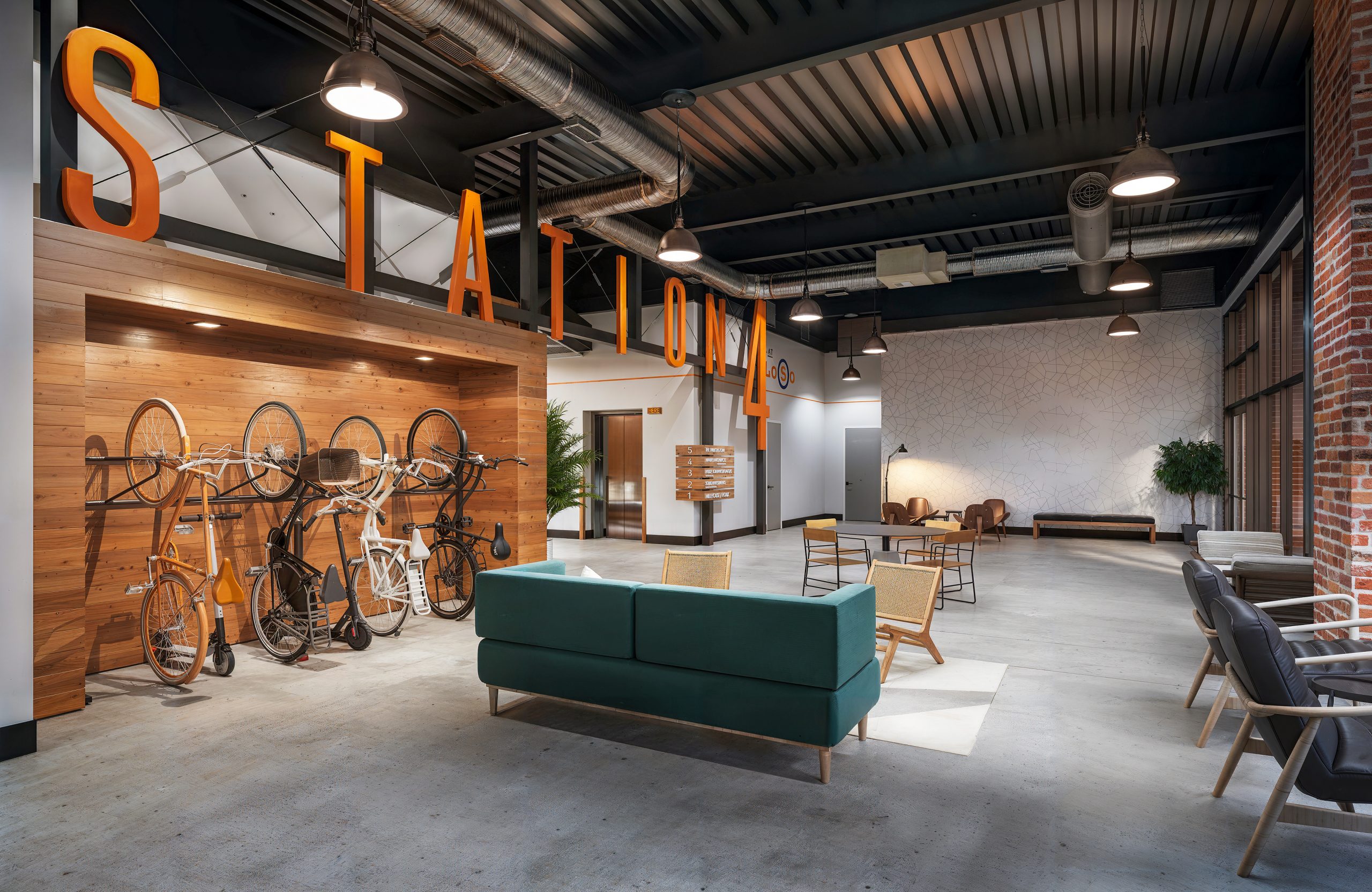 Station 4 at The Station at LoSo Charlotte lobby and lounge interior rendering by Bogza.com. A spacious industrial-chic communal area featuring a large orange