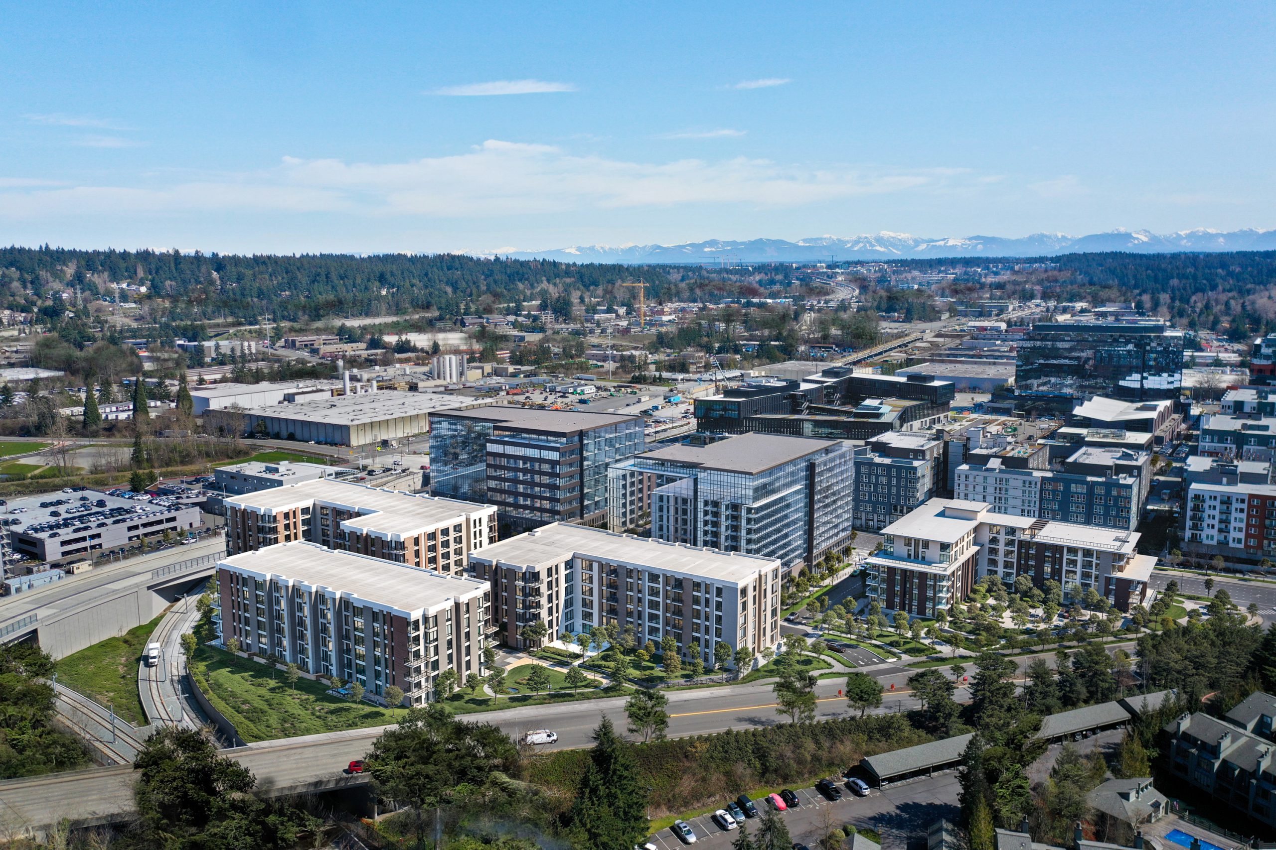 12th Place Development Bellevue residential aerial architectural rendering by Bogza.com. A focused view of the mid-rise apartment buildings featuring landscaped courtyards, set against adjacent glass office towers and distant mountain ranges.