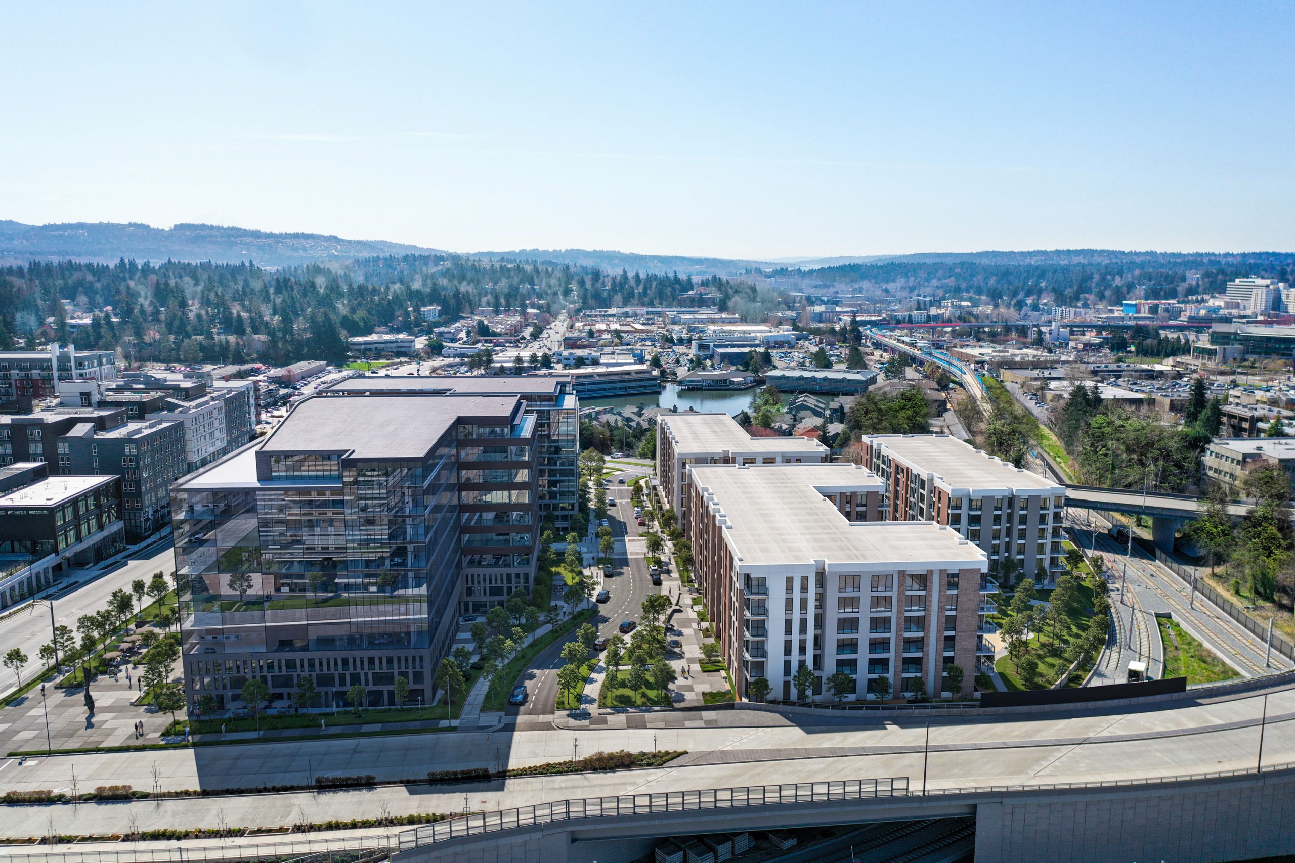 12th Place Development Bellevue mid-level aerial architectural rendering by Bogza.com. The view highlights the landscaped pedestrian street and public plaza separating modern glass office buildings from residential apartments alongside the light rail line.