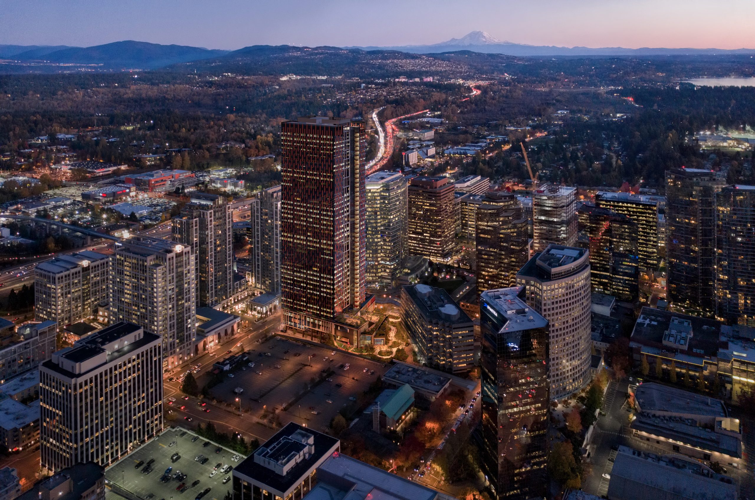 600 Bellevue aerial architectural rendering by Bogza.com. A breathtaking dusk view over the Bellevue skyline showcasing the illuminated 31-story high-rise office tower with a distant view of Mount Rainier.