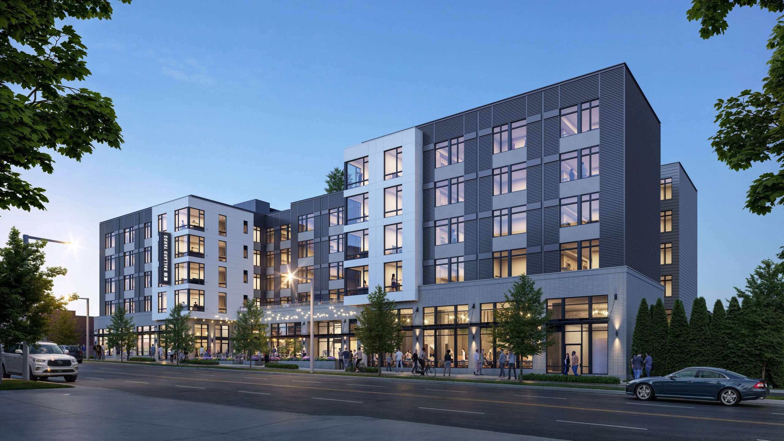 Ballard Yards Seattle street-level architectural rendering by Bogza.com. A twilight view showcasing the building's maritime-industrial inspired facade, warm ground-floor retail spaces, string lights, and neighborhood pedestrian activity.