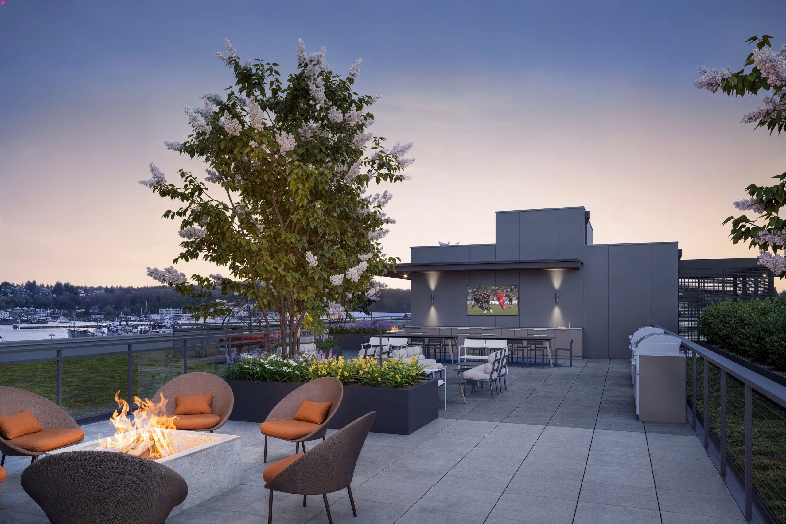 Ballard Yards Seattle rooftop deck amenity rendering by Bogza.com. A luxurious outdoor terrace at twilight featuring a fire pit, comfortable lounge seating, an outdoor TV, BBQ grills, and distant views of the harbor.