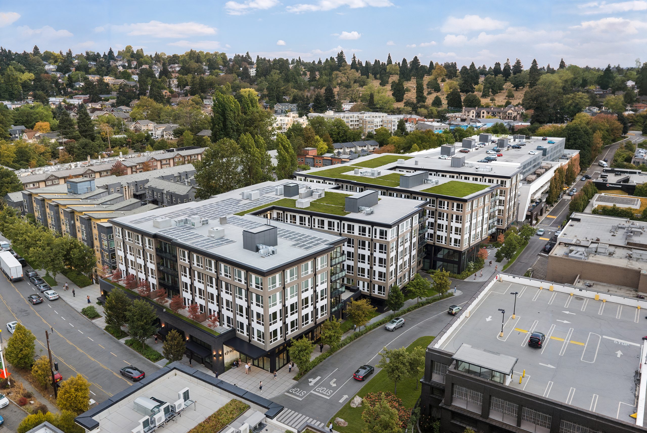 Broadstone Strata Seattle aerial architectural rendering by Bogza.com. A high-angle drone view of the expansive 7-story mixed-use development in the Ravenna neighborhood, highlighting the multi-wing building structure, green roofs with solar panels, internal courtyards, and surrounding urban landscape.
