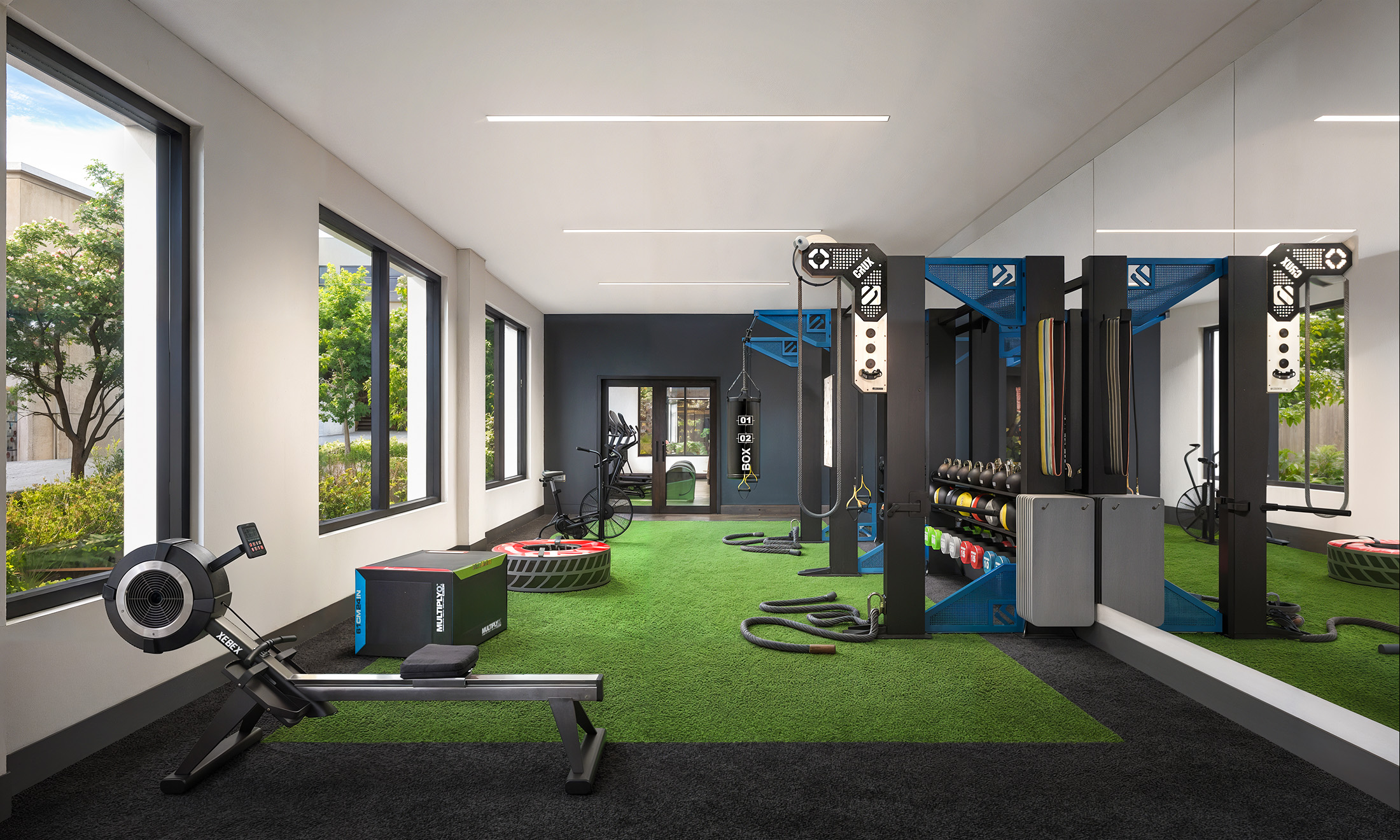 Broadstone Strata Seattle HIIT and on-demand fitness studio interior rendering by Bogza.com. A dedicated athletic training space featuring indoor green turf, a rowing machine, a punching bag, free weights, and cross-training equipment set against a large mirror.