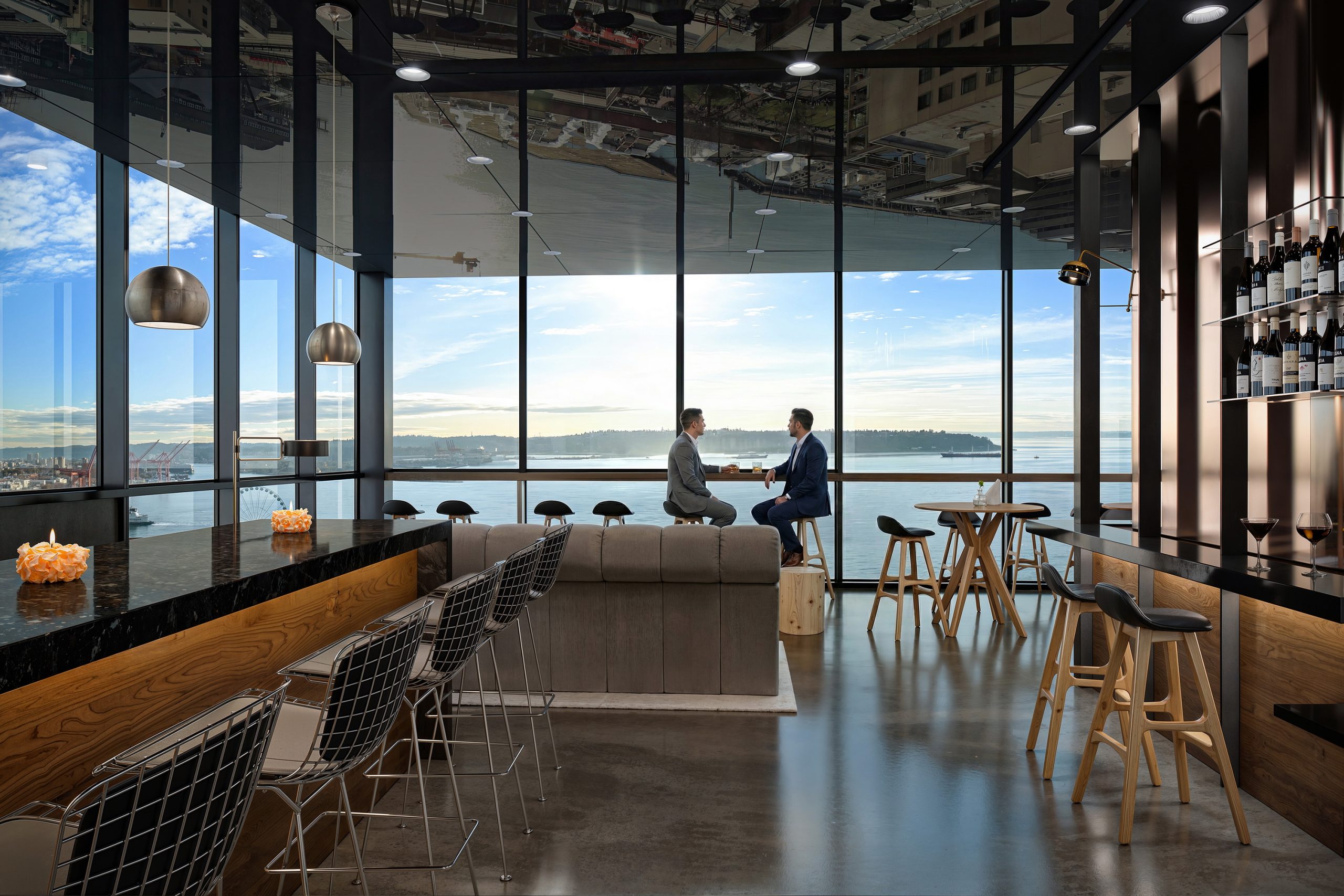 Thompson Seattle Hotel The Nest rooftop bar interior rendering by Bogza.com. A sophisticated high-rise lounge featuring a long marble bar, modern seating, warm wood accents, and expansive floor-to-ceiling windows framing panoramic views of Elliott Bay.
