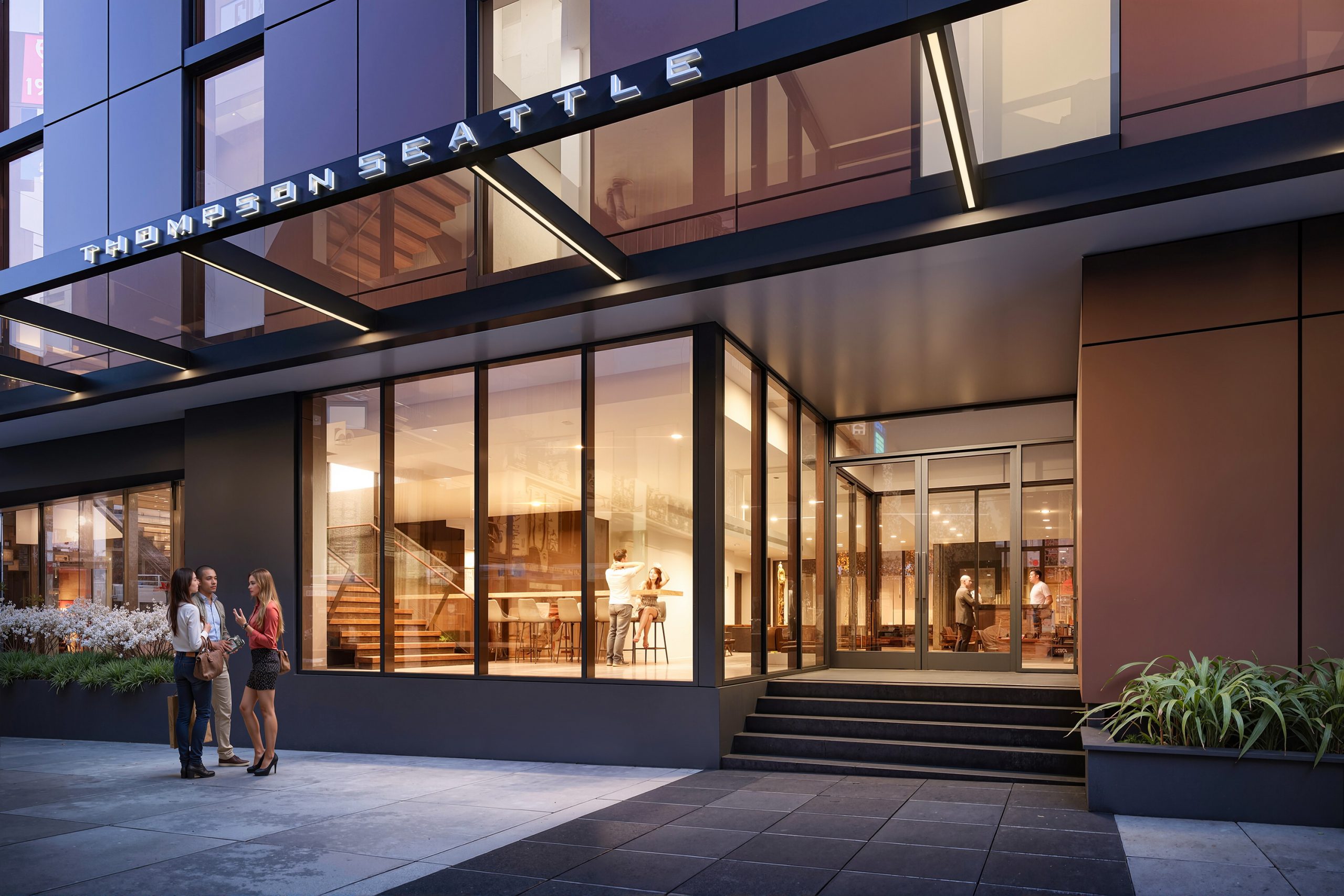 Thompson Seattle Hotel street-level exterior architectural rendering by Bogza.com. A glowing dusk view of the luxury boutique hotel's main entrance and ground-floor restaurant, featuring expansive floor-to-ceiling windows, warm interior lighting, and modern signage along 1st Avenue.