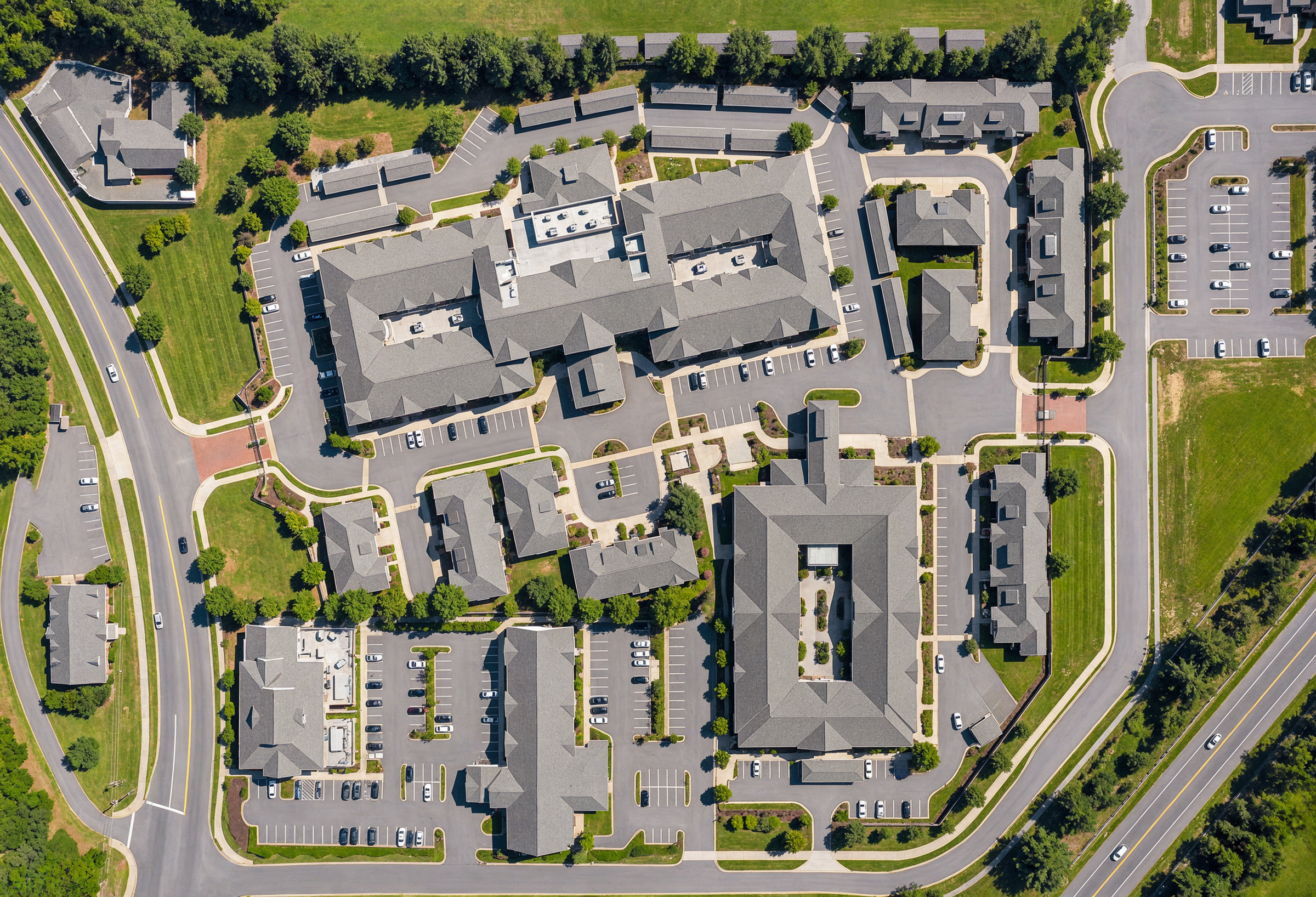 University Village retirement community aerial site plan rendering by Bogza.com. A direct top-down bird's-eye view of the sprawling senior living development, highlighting the complex building footprints, landscaped courtyards, parking areas, and surrounding roads.
