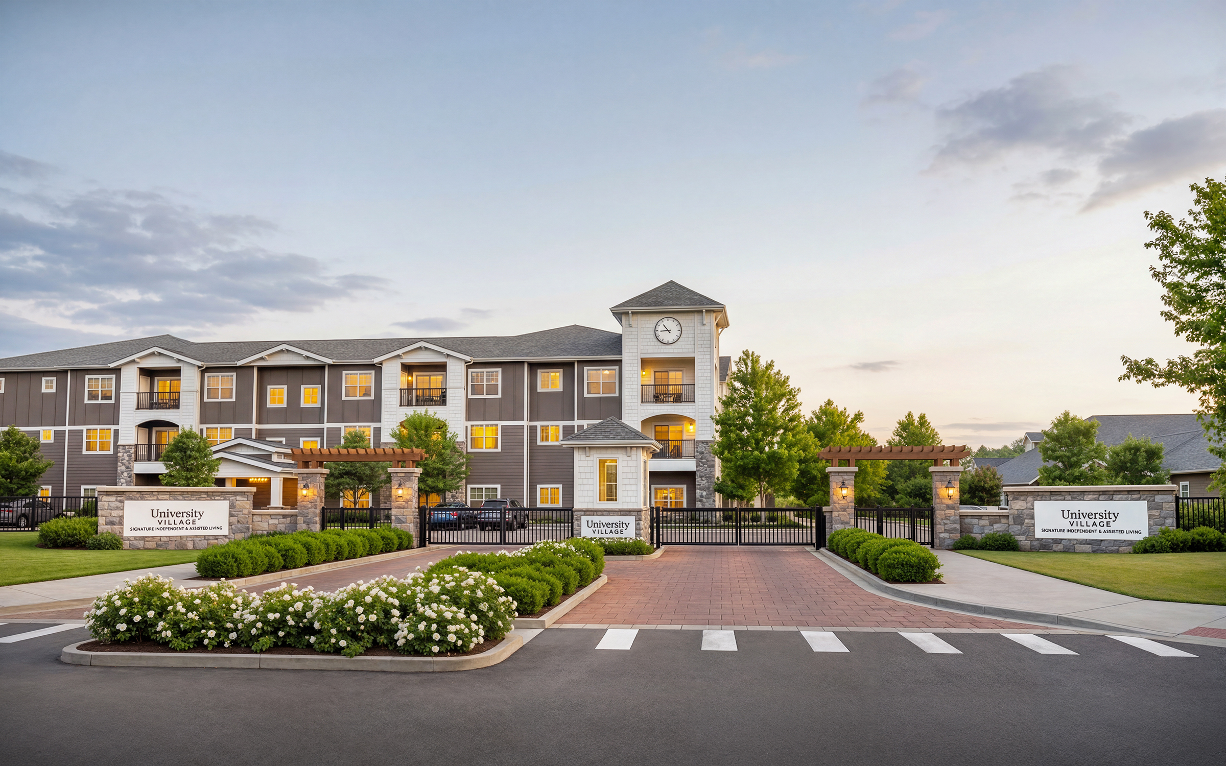 University Village senior living gated entrance architectural rendering by Bogza.com. A bright sunset view of the community's secure entrance drive, featuring a classic brick pathway, manicured hedges, the main multi-story residential building, and a prominent clock tower.