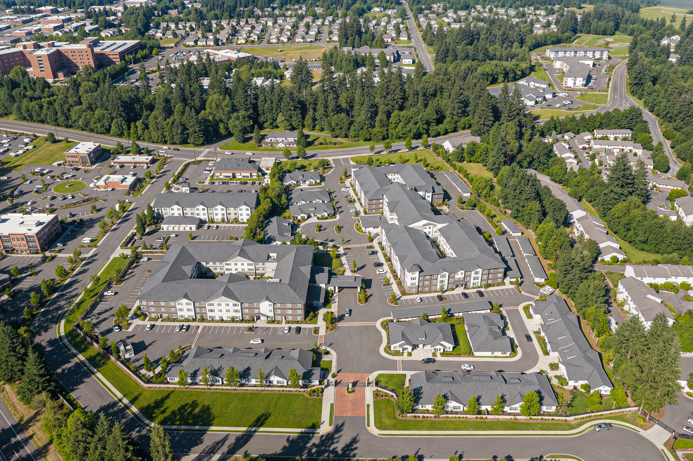 University Village senior living community aerial architectural rendering by Bogza.com. A high-angle daytime drone view of the expansive luxury retirement campus, showcasing interconnected residential wings, internal courtyards, standalone cottages, and surrounding neighborhood trees.