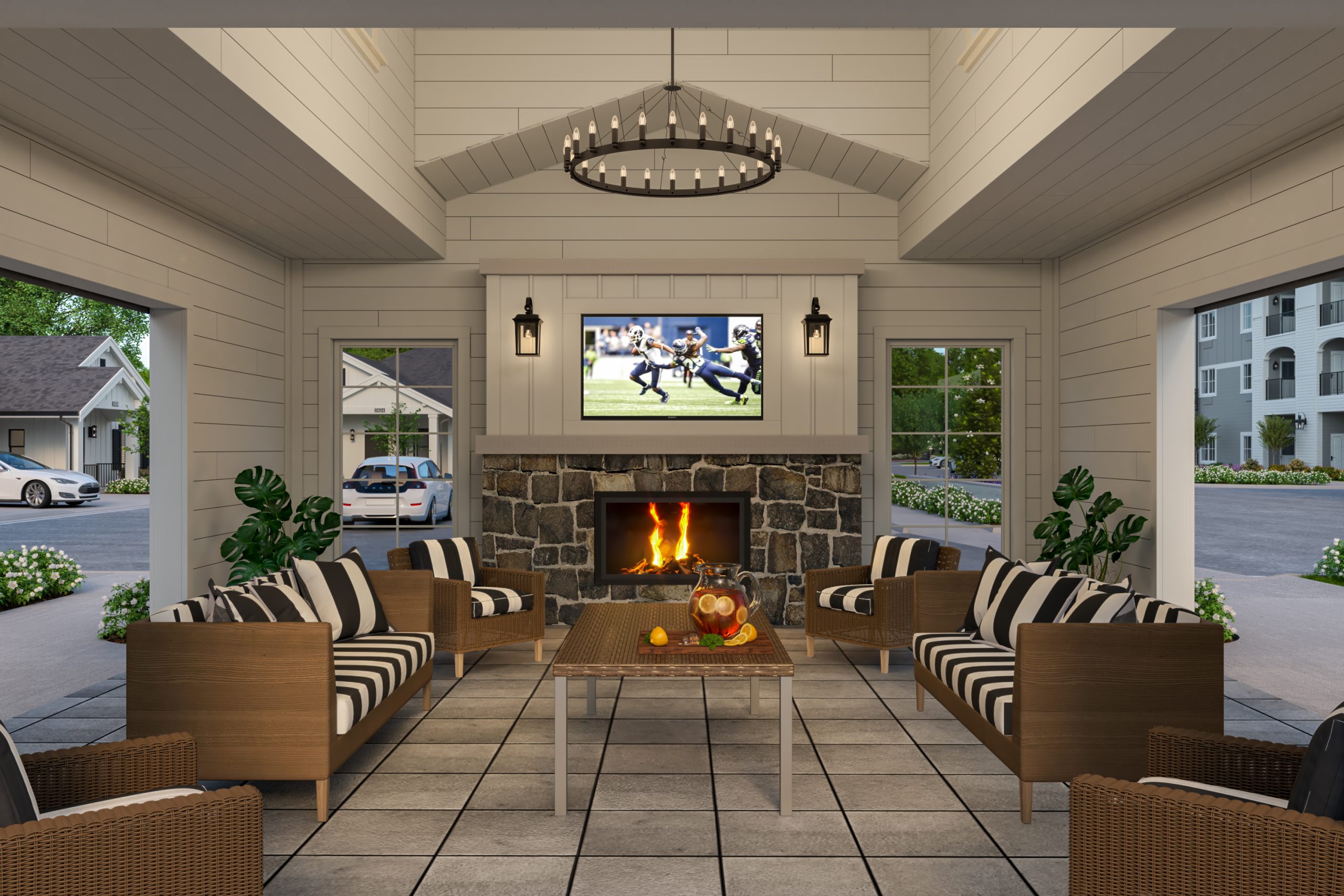 University Village senior living covered outdoor patio lounge architectural rendering by Bogza.com. A cozy, open-air communal seating area featuring a rustic stone fireplace, a flat-screen TV showing sports, comfortable wicker furniture with striped pillows, and an exposed wood ceiling.