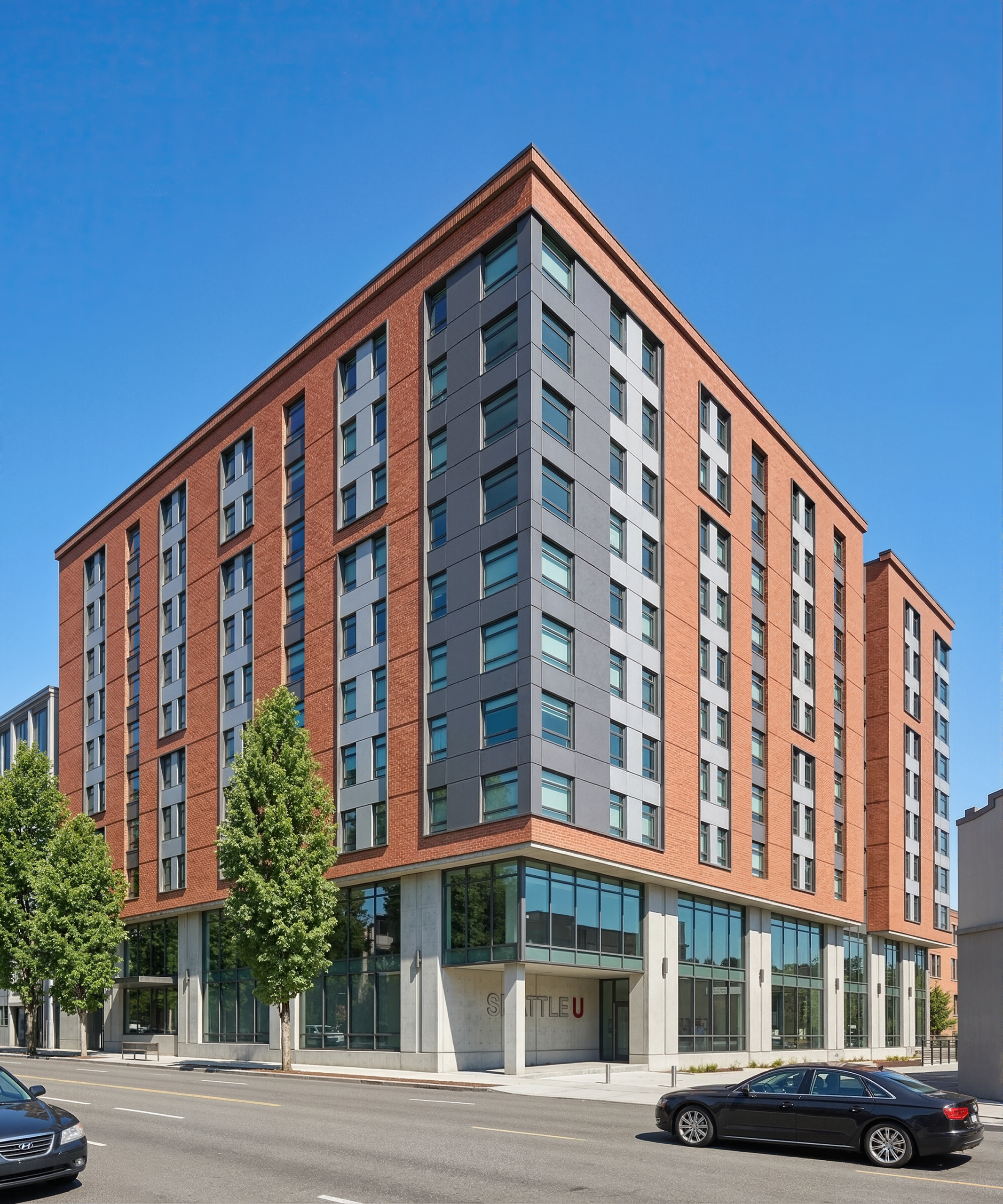 Vi Hilbert Hall Seattle U exterior architectural rendering by Bogza.com. A daytime view from across the street showcasing the 10-story student housing development, highlighting the red brick and metal facade, street trees, and the 