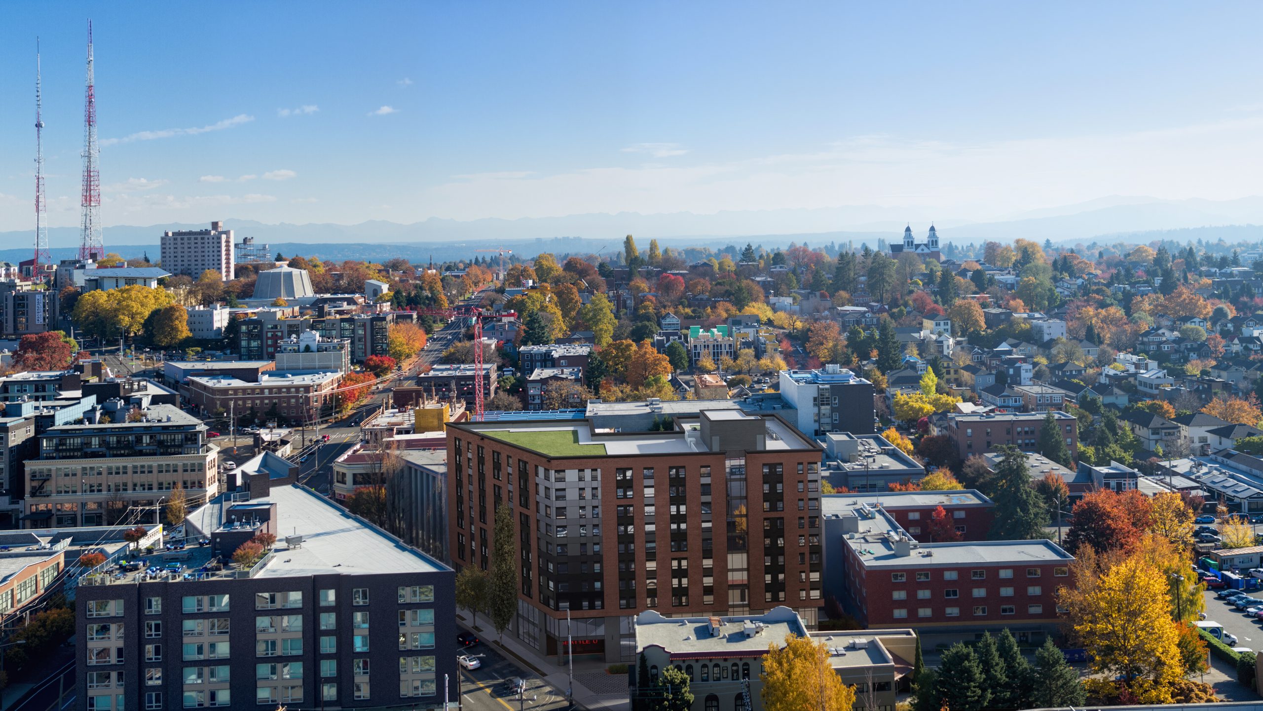 Vi Hilbert Hall Seattle University aerial architectural rendering by Bogza.com. A high-angle drone view of the modern 10-story student apartment building, showcasing the green roof terrace, autumn trees, and sweeping views of the Capitol Hill neighborhood and distant mountains.